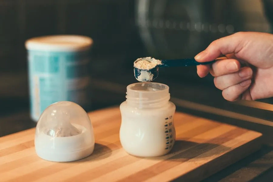 man scooping infant formula into bottle